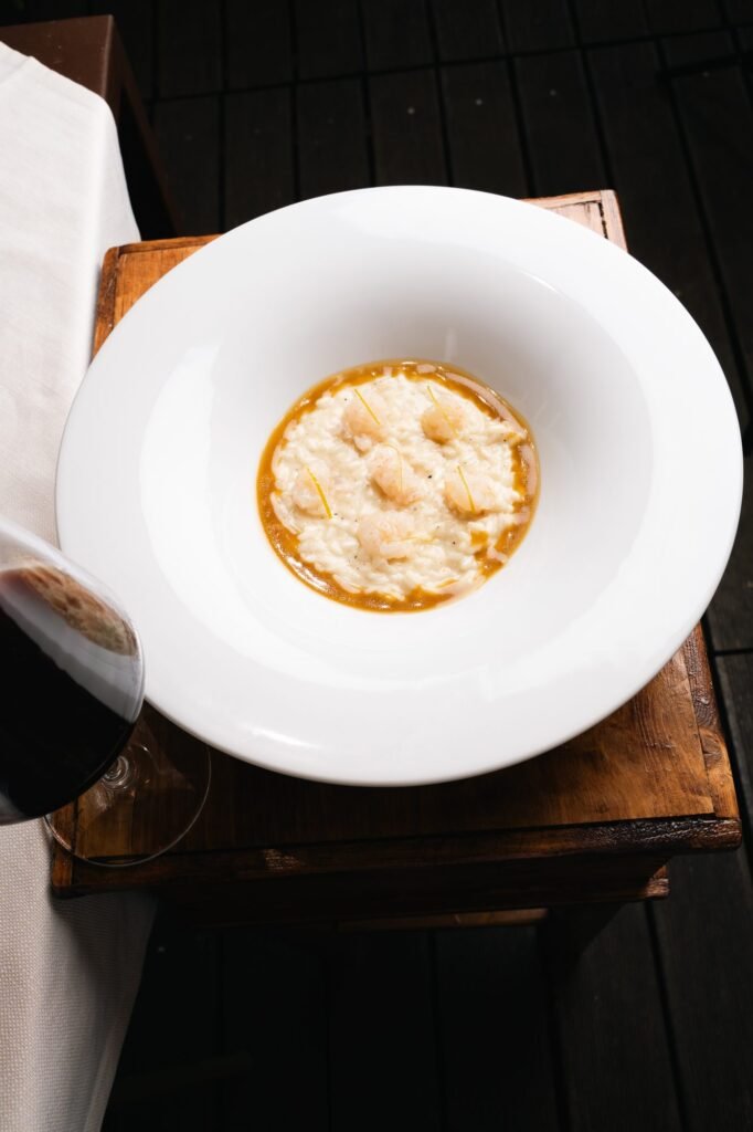 Risotto ai gamberetti impiattato e fotografato dall'alto su una cassettina di legno, con a fianco il bicchiere di vino rosso