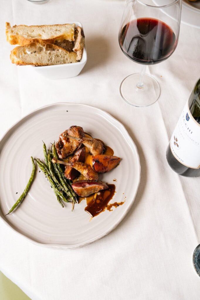 Plate of meat with crisp green beans served at the table with estate bottle